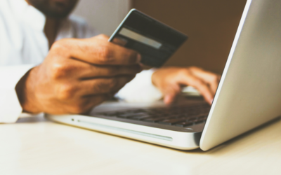 Close up on a man's hands on a keyboard holding a credit card in one hand and typing with the other.